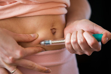 Woman making hormonal therapy injection into her belly. Close up syringe pen. Person in bedroom, in vitro fertilisation treatment. - obrazy, fototapety, plakaty