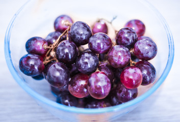 Fototapeta na wymiar Blurred glass bowl with purple grapes. Selective focus.