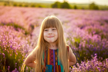 happy childhood. Laughing girl builds faces, dabbles. Barren child in a field of lavender at sunset. backlight Sun rays.