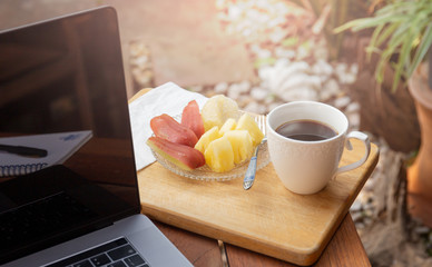 Coffee mug with fresh fruit and laptop on wooden table in the garden.