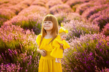 happy childhood. Favorite toys. Girl with a doll in a lavender field. Pampering, emotions, joy. Sunset