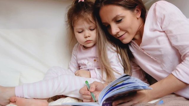 Cute young mother paints coloring with her little daughter. The concept of educational activities with children