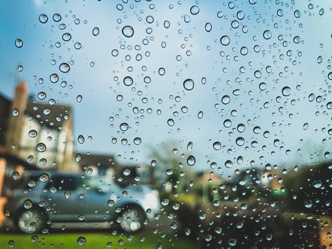 Droplets Of Rain On The Window And Windshield Of A Car O A Sunny Day - View Of A House And Neighbourhood Through It.