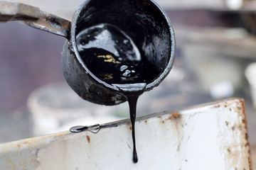 Melted hot  black tar from metal cup on surface with steam