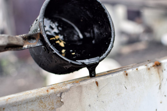 Outflow of melted hot  black tar from metal cup on surface with steam