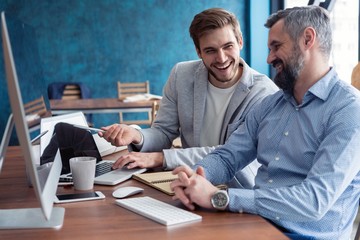 Shot of two business colleagues working in their office using a desktop computer. Man sitting at...