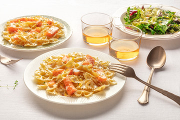 Pasta and wine, Italian dinner. Farfalle with smoked salmon and cream sauce, served with mesclun salad leaves