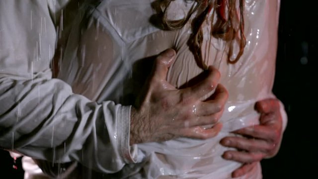 Couple in light wet clothes in the dark in the rain. Close - up of male hands on the back of the girl. Hands grip the back of the girl. Dripping drops
