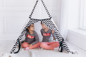 Two positive cheerful girls playing together at home with toys in children wigwam. Friendship, childhood, happiness concept © Andreshkova Nastya