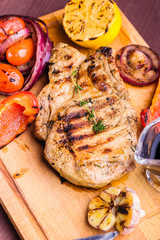 Juicy pork steak with a sprig of fresh thyme, lemon and grilled vegetables and sauce served on a wooden board. Top view