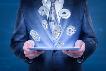 Crop close-up of businessman's chest and hands holding thin tablet lighting up some cogwheels flying above it.