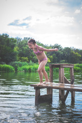 Little cute girl jumping off the dock into a beautiful river at sunset