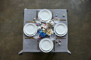 top view of table with white plates, cutlery, crystal glasses, cutlery, painted eggs and flowers at home