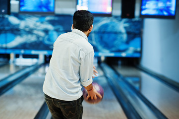 Back of asian man in jeans shirt standing at bowling alley with ball on hands and throw it.