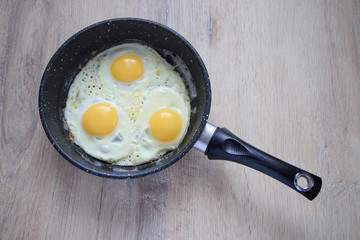 fried eggs in a pan on a wooden board background