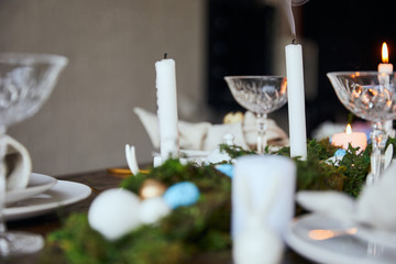 selective focus of candles, green moss and crystal glasses on wooden table at home