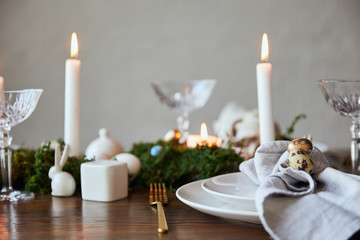 selective focus of quail eggs on napkin and plates near green moss, candles and crystal glasses on wooden table at home