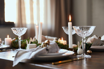 selective focus of burning candles near plates and crystal glasses on wooden table at home