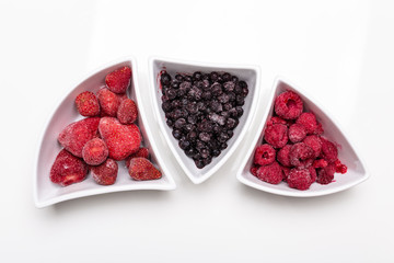 ripe berries in shaped white bowls on white background