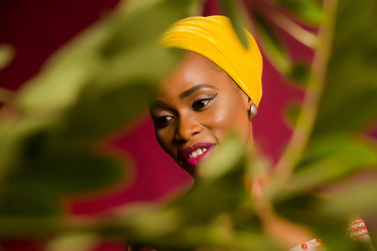 Portrait of a lady wearing yellow scarf on red background with some blurred flowers in the foreground. 