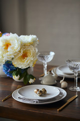Selective focus of quail eggs on white plates, flowers and crystal glasses on wooden table at home