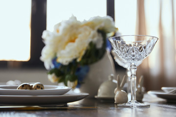 selective focus of crystal glass, bouquet in vase and decorative rabbits on wooden table at home