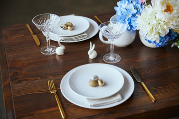 crystal glass, flowers in vase, golden cutlery and decorative rabbits on wooden table at home
