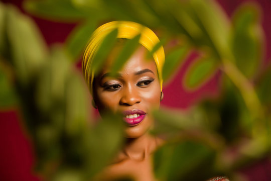 Portrait of a lady wearing yellow scarf on red background with some blurred flowers in the foreground. 