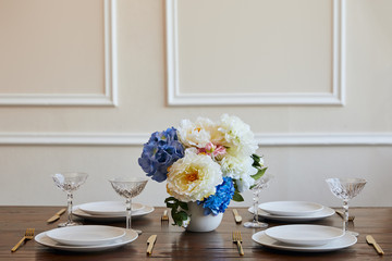 white plates, golden knifes and forks, crystal glasses and flowers in vase on wooden table in restaurant