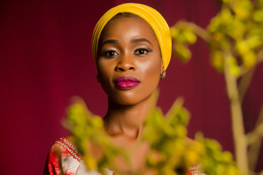 Portrait of a lady wearing yellow scarf on red background with some blurred flowers in the foreground. 