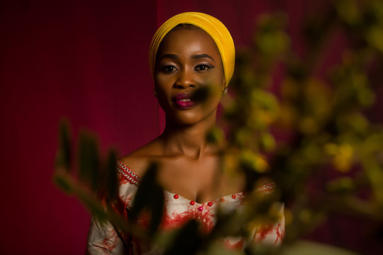 Portrait of a lady wearing yellow scarf on red background with some blurred flowers in the foreground. 
