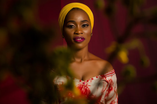 Portrait of a lady wearing yellow scarf on red background with some blurred flowers in the foreground. 