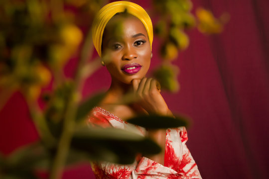Portrait of a lady wearing yellow scarf on red background with some blurred flowers in the foreground. 