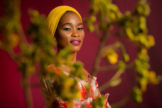 Portrait of a lady wearing yellow scarf on red background with some blurred flowers in the foreground. 