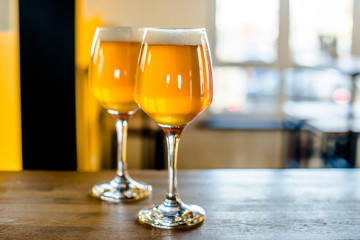 Two glasses of beer are on the bar table. 