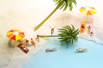 Summer on the beach. Miniature people sunbathing, running, swimming on the beach with umbrellas and coconut trees. Holiday, vacation, travel and leisure concept