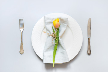 Easter table setting with yellow tulip on pastel blue. Top view.