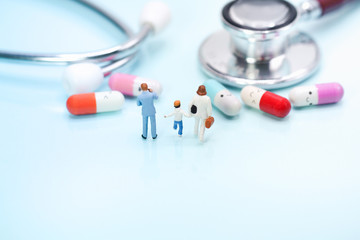 Miniature people: family standing in front of colorful pills and stethoscope on blue background with copy space. Health care, medical service, and insurance concept