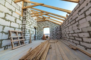 Fototapeta premium House interior under construction and renovation. Energy saving walls of hollow foam insulation blocks and bricks, ceiling beams and roof frame.