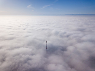 Aerial top view of foggy cloudy landscape with radio or TV antenna top on blue sky copy space background and mountain ridge on horizon.