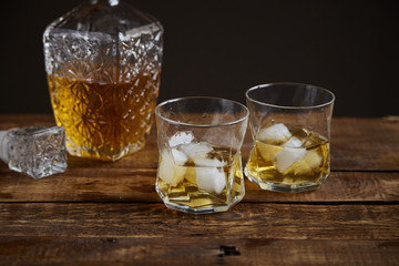 Whiskey with ice in glasses, rustic wood background, copy space 