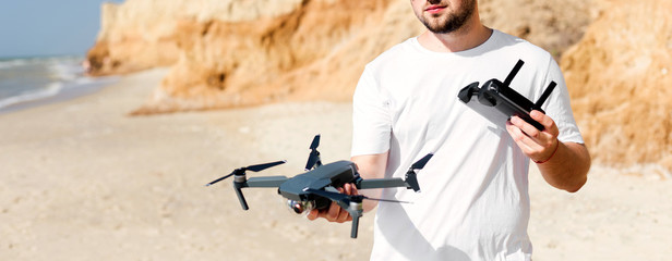 Young man holding drone before flight near ocean or sea. Pretty guy prepare to pilot outdoor