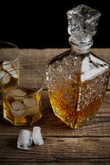 Whiskey with ice in glasses, rustic wood background, copy space 