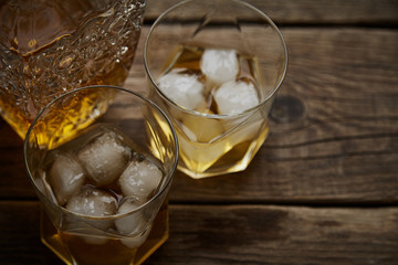 Whiskey with ice in glasses, rustic wood background, copy space 