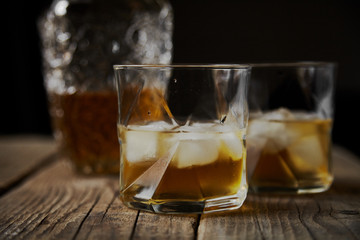 Whiskey with ice in glasses, rustic wood background, copy space 