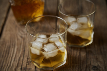 Whiskey with ice in glasses, rustic wood background, copy space 