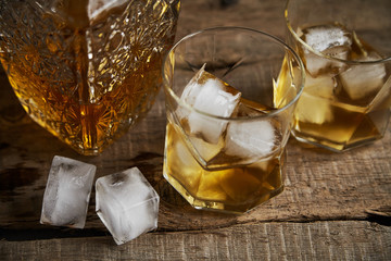 Whiskey with ice in glasses, rustic wood background, copy space 