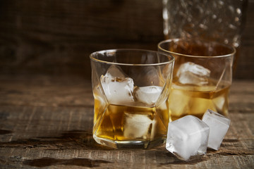 Whiskey with ice in glasses, rustic wood background, copy space 