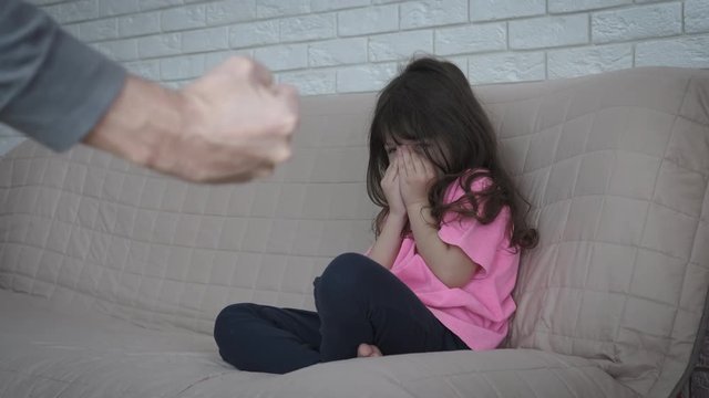 Domestic violence. Child abuse. A little girl in fear covers her face with her hands when her father threatens her with his fist.