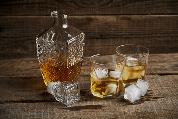 Whiskey with ice in glasses, rustic wood background, copy space 